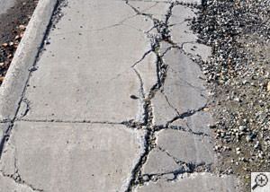A severely damaged, sinking sidewalk with washed out sand underneath in Whitestone.