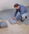 Contractors installing basement subfloor tiles and matting on a concrete basement floor in Flushing, New York